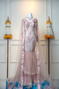 Karmaşık dantel işlemeli ve akışkan tül trenli göz kamaştırıcı bir pastel gelinlik, bir manken üzerinde sergileniyor, zarafet ve romantik karmaşıklık yayıyor..