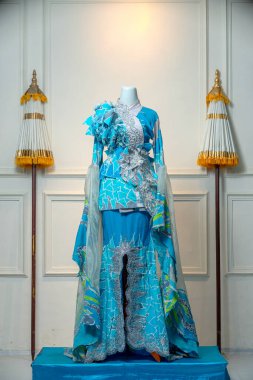 Altın dekoratif şemsiyeler arasındaki mankende sergilenen çiçek ve dantel süslemeli zarif turkuaz elbise düğün, akşam ve kültürel kutlamalar için mükemmeldir..