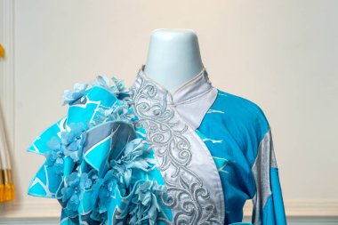 Karmaşık gümüş işlemeli zarif mavi bir elbise ve 3 boyutlu çiçek aksanlı, düğünler veya özel etkinlikler için tasarlanmış, sofistike ve sanatsal yetenekler yayıyor..