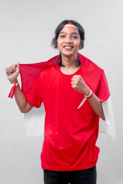 Genç bir Endonezyalı vatansever ulusal bayrağı tutarken gururla bağırıyor, kırmızı ve beyaz aksesuarlar takıyor ve Endonezya Bağımsızlık Günü 'nü tam bir ruhla kutluyor..