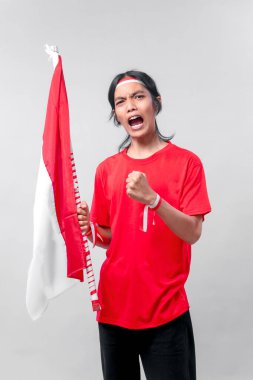 Tutkulu Endonezyalı genç adam Bağımsızlık Günü 'nde ulusal bayrağı tutarken bağırıyor ve yumruğunu kaldırıyor, güçlü duygu ve vatanseverlik duygusu gösteriyor..