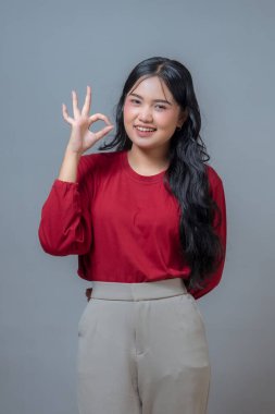 Uzun siyah saçlı Endonezyalı kadın sessiz sessiz bir jest yapıyor, parmakları dudaklarında, hafifçe öne eğiliyor, neşeli bir ifadeyle gülümsüyor.