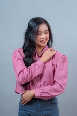 Genç Endonezyalı bir kadının portresi. Uzun siyah saçlı, pembe tişörtlü, gözleri kapalı, omuzları omuzlarında gülümseyen, sakinliğini ve duygusal sıcaklığını ifade eden..