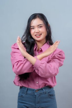 Pembe tişörtlü Asyalı bir kadının portresi. X şeklinde bir jest yapmak için kollarını kavuşturuyor. Reddetme ya da yasağı ifade ediyor..