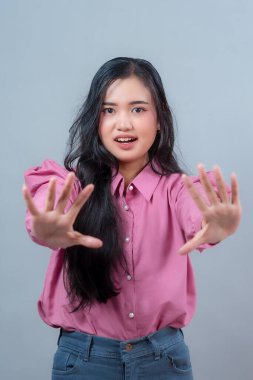 Endonezyalı, uzun siyah saçlı, pembe tişörtlü bir kadın. İki elini de bir dur hareketiyle öne doğru gösteriyor. Reddettiğini ya da uyardığını belirtiyor..