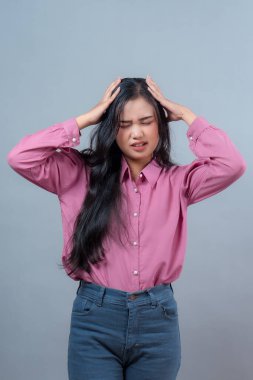 Pembe gömlek giyen Endonezyalı genç bir kadının portresi, gözlerini kapatıyor ve başını dertten tutuyor. Migren, baş ağrısı, endişe, hayal kırıklığı ya da zihinsel aşırı yüklenme kavramı.