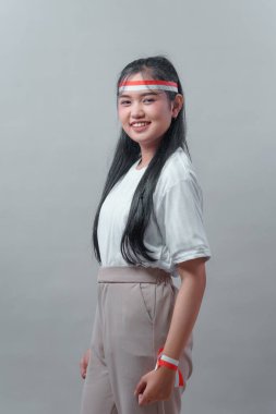 Endonezyalı bir kadın kendine güvenen bir gülümseme ile beyaz gömlek ve yumuşak pantolonla poz veriyor, ulusal gururunu göstermek için kırmızı ve beyaz aksesuarlar takıyor..