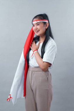 Uzun siyah saçlı neşeli bir Endonezyalı kadın ulusal bayrağı tutuyor ve gururla gülümsüyor. Bağımsızlık Günü 'nde vatansever ruhunu ve mutluluğunu ifade ediyor..