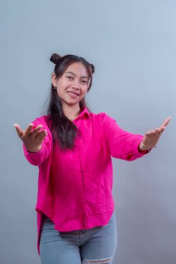 Uzay çörekleri olan, pembe gömlek giyen, gülümseyen ve iki eliyle uzanan Endonezyalı genç bir kadın. Stüdyo ortamında dostane bir jest, olumlu ve misafirperver bir hava..