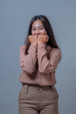 Endonezyalı bir kadın bu fotoğrafta kendini neşeyle ifade ediyor. Kameraya sımsıkı gülümserken neşeli bir hareketle ellerini yüzünün yanında tutuyor..