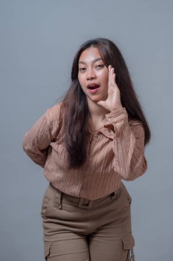 Bej gömlekli genç Endonezyalı bir kadın, bir eli ağzında duruyor, sanki bir sırrı ya da anonsu paylaşıyormuş gibi, anlamlı ve canlı bir yüzle. Yaratıcı kavramlar için mükemmel.