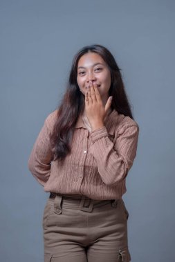 Endonezyalı genç bir kadının portresi utangaç bir şekilde gülümseyerek ağzını kapatıyor. Stüdyoda hoş ve anlamlı bir jest sergiliyor..