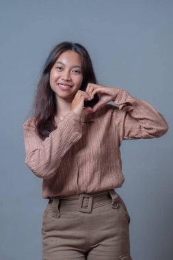 Elleriyle kalp şekli yapan gülümseyen Endonezyalı bir kadın sıcaklığını, şefkatini ve pozitifliğini iletiyor. Onun dostça ifadesi ve hareketi reklam ve küresel pazarlama için idealdir..