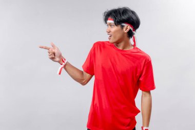 Kırmızı tişörtlü enerjik genç Endonezyalı adam Bağımsızlık Günü 'nü gururla ve coşkuyla kutlamak için kırmızı ve beyaz aksesuarlar takıyor..