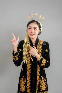 Geleneksel Cava kebaya ve karmaşık altın aksesuarlar takan güzel, genç Asyalı bir kadın, güvenli bir şekilde gülümserken anlamlı ve çekici bir yüz ifadesi takınıyor..