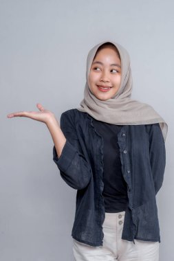 Bir yandan yan bakarken tesettürdeki gülümseyen Asyalı Müslüman bir kadının portresi, kopya alanı kullanımı için boş bir arka planla stüdyoda güvenle duruyor..