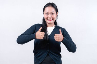 Siyah hırkalı gülümseyen bir Asyalı kadın, uzun siyah saçlı, tarafsız bir arkaplana karşı elleriyle baş parmak işareti yapıyor..