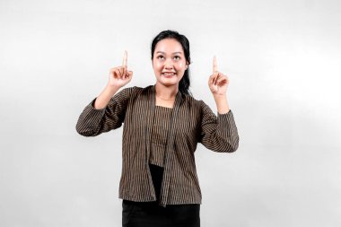 Geleneksel Lurik giysiler giyen Endonezyalı bir kadın, iki elini de işaret parmaklarıyla havaya kaldırarak, tarafsız bir arka plana karşı kültürel gurur ve coşku gösterirken parlak bir şekilde gülümsüyor.