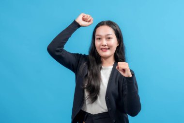 Neşeli genç bir kadın, parlak mavi bir arka plana karşı yumruklarını kaldırarak sevinç ve coşku dolu bir şekilde kutluyor..