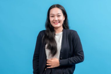 Uzun siyah saçlı, hırka giyen, gülümseyen ve mavi arka planda poz veren neşeli bir kadın. Görüntü mutluluğu, güveni ve gündelik tarzı canlı bir zemin ile yakalıyor..