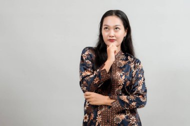 Endonezya 'nın zarif batik giysileri içinde düşünceli genç bir kadın. Düşünceli bir ifadeyle çenesine dokunuyor, fikirleri yansıtıyor ve geleneksel modanın güzelliğini sergiliyor.