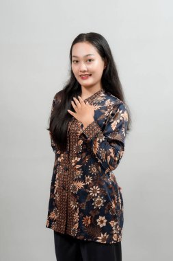 Endonezya 'nın şık batik kıyafetli çekici genç bir kadın elini göğsüne koyup gülümseyerek geleneksel modanın güzelliğini ve zarafetini sergiliyor..