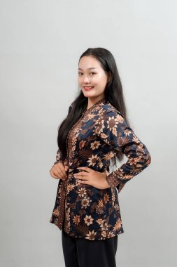 Şık batik kıyafetli kendine güvenen genç bir kadın, neşeli bir gülümseme ve elleri kalçasında poz veriyor, modern Endonezya modasının ruhunu somutlaştırıyor..