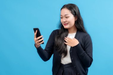 Mutlu genç bir kadın akıllı telefon kullanıyor, neşeyle gülümsüyor, bağlantıyı, modern iletişimi ve teknolojiyi sembolize ediyor, canlı mavi bir arka plana karşı.