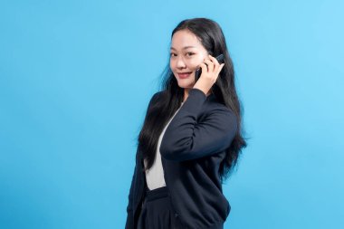 Akıllı telefonda canlı mavi arka planda konuşurken gülümseyen profesyonel bir kadın. İletişim, iş, bağlantı ve modern teknolojiyi sembolize eder.