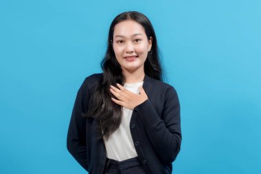 Samimi bir ifadeye sahip genç bir kadın ellerini göğsüne koyuyor, sağlam mavi bir arka plana yaslanıyor, minnettarlığını, takdirini ya da samimi duygularını ifade ediyor..