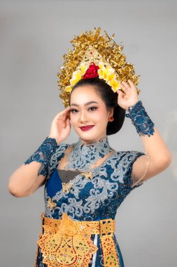 Çekici gülüşü ve kendine güveni olan Asyalı kadın, zarif modern Balili kostümü ve altın çiçekli başlık takıyor, zarif poz veriyor..