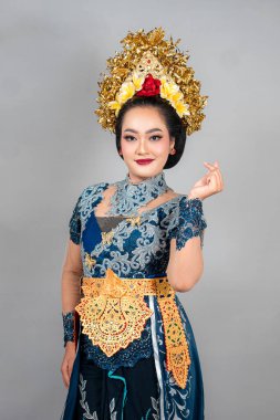 Modern Bali geleneklerine uygun giyinmiş güzel bir Asyalı kadın sıcak, büyüleyici bir gülümsemesi ve reklam görselleri için mükemmel bir yüz ifadesiyle kendine güvenen bir parmak hareketi yapıyor..