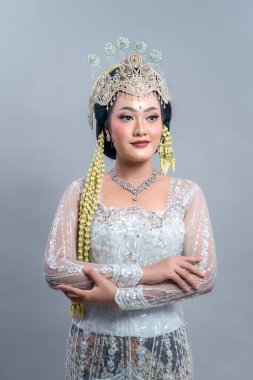 Geleneksel Endonezyalı bir gelin, süslenmiş bir taç, çiçek aksesuarları, detaylı kebaya ve zarif bir makyajla kendine güvenle yan tarafa bakar..