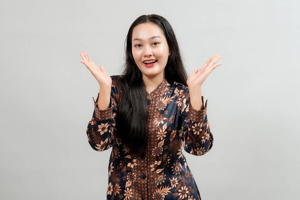 Заинтересованная молодая женщина в яркой индонезийской одежде батик, с открытыми руками и радостным выражением лица, передающая волнение, удивление или представляющая что-то большое.