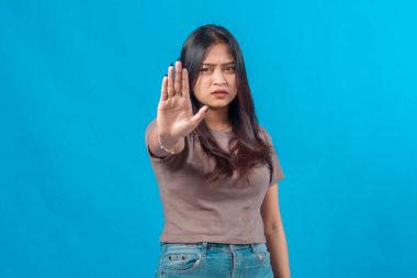 Asyalı genç bir kadın elini kaldırarak ciddi bir ifade sergiliyor. Mavi bir arkaplan karşısında dur işareti yapıyor. Reddedilme ya da uyarı işareti..