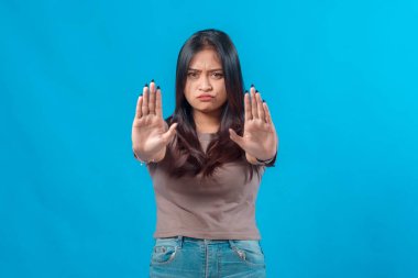 Genç Asyalı kadın iki eliyle birden çifte duruş hareketi yapıyor. Ciddi ve iddialı bir yüz ifadesi sergiliyor. Stüdyo ortamında canlı, mavi bir arka plana karşı duruyor..