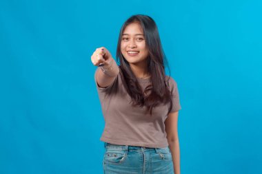 Gülümseyen genç Asyalı kadın kameraya özgüvenle bakıyor, günlük kıyafetler giyiyor ve düz mavi bir arkaplanda duruyor. Pazarlama ya da işe alım reklamları için ideal.