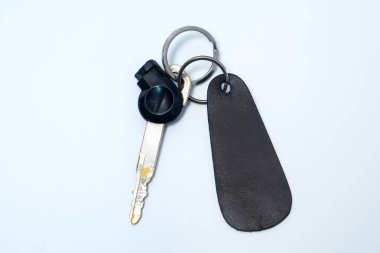 Siyah plastik başlı ve deri anahtarlıklı bir motosiklet anahtarı beyaz bir arka plana yerleştiriliyor, bu da güvenlik, ulaşım, mülkiyet ve kişisel eşyaları sembolize ediyor..