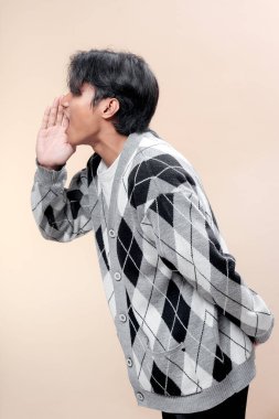 Asyalı adam gri baklava desenli hırka giymiş, el ele tutuşmuş, bağırıyor gibi, etkileyici iletişim ve kendine güvenen tavırlar sergiliyor..