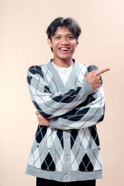 Gülümseyen Asyalı genç bir adam desenli bir süveter giyiyor ve kendine güvenen bir şekilde yana bakıyor, iş, reklam, yaşam tarzı, iletişim ve tanıtım temaları için ideal..