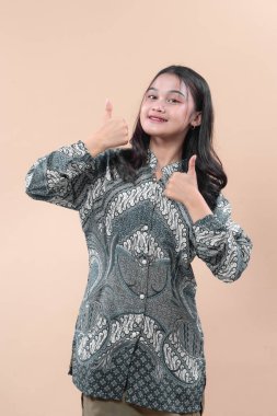 Batik giysili Asyalı bir kadın iki baş parmağını kaldırarak gülümseyerek onay, başarı, olumlu duygu, kültürel kimlik ve zarafeti temsil ediyor..