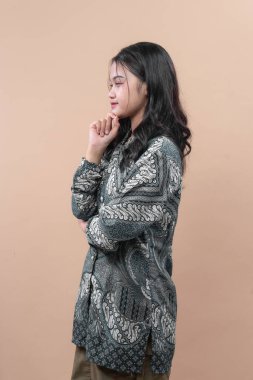 Zarif batik kıyafetler giyen Asyalı kadın çene ve düşünceli yüz ifadeleriyle yan yana poz veriyor. Tarafsız arka planda özgüven, kültür ve profesyonel tarzı gösteriyor..