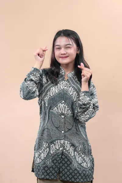 Zarif batik tişörtlü gülümseyen Asyalı kadın iki eliyle parmak kalp hareketi gösteriyor, neşe, pozitiflik, kültürel gurur ve küresel reklam kavramlarına olan güveni ifade ediyor..