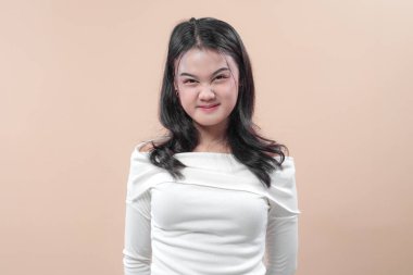 Beyaz omuzlu, uzun siyah saçlı Asyalı bir kadın. Burnu buruşmuş bir şekilde gülümsüyor. Sade arka planda oyuncu ve kendinden emin görünüyor..