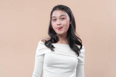 Beyaz omuzlu, uzun siyah saçlı Asyalı kadın, arka planda şakacı ve komik bir ifadeyle dilini hafifçe dışarı çıkarıyor..