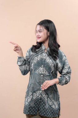 Batik desenli bir tişört giyen Asyalı bir kadın, kendine güvenen bir gülümsemeyle, iş iletişimini, zarafeti ve kültürel kimliği temsil ediyor..