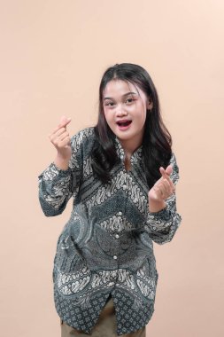 Zarif batik tişört giyen genç Asyalı kadın neşeli bir kalp hareketi yapıyor, neşe, güven, pozitiflik ve kültürel kimliğini doğal cazibe ve modern tarz ile ifade ediyor..