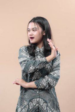 Zarif batik kıyafetli Asyalı bir kadın, etkileyici el hareketleriyle, kendine güveni bir yana bakıyor, iletişimi, tutumu ve kültürel profesyonelliği simgeliyor..