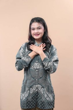 Zarif batik gömlek giyen Asyalı bir kadın ellerini göğsüne koyuyor, içten gülümsüyor, minnettarlığı, saygıyı, kültürel gururu ve pozitif tutumu simgeliyor..