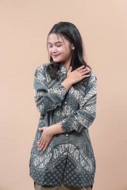 Geleneksel batik kıyafetler giyen Asyalı bir kadın. Göğsünde sakin bir gülümseme ve el hareketi var. Minnettarlık, güven, zarafet ve kültürel kimlik gösteriyor..